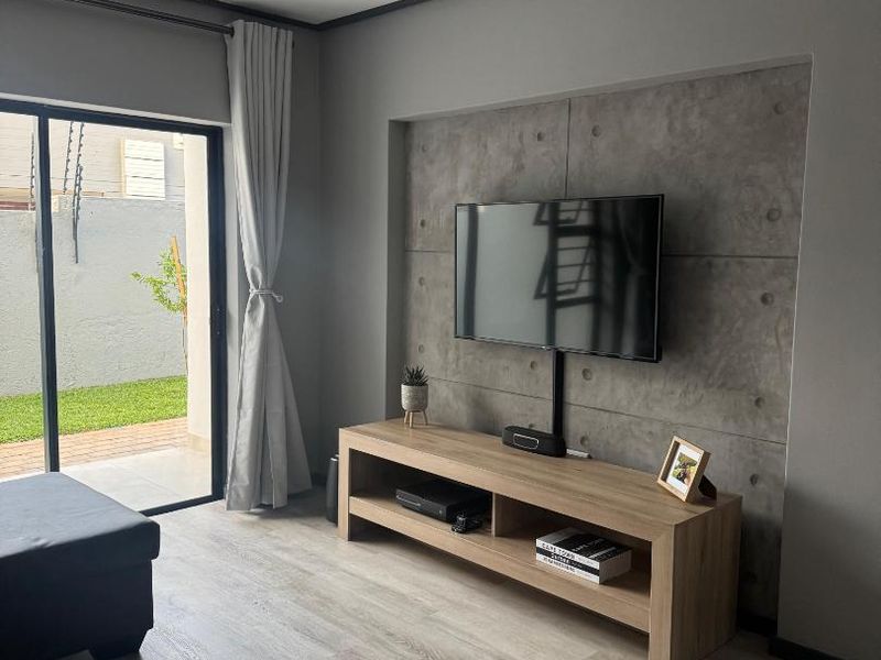 Modern living room featuring a concrete accent wall, light laminate flooring, and a sliding glass door providing access to the outdoor area.