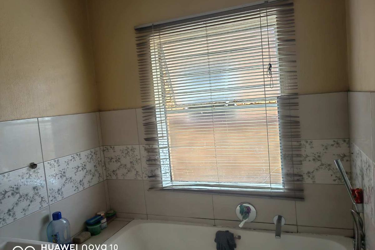 A bathroom featuring a built-in bathtub with wall-mounted fixtures and a window with horizontal blinds.