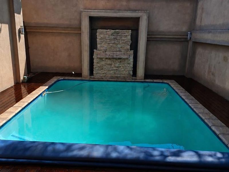 Private courtyard featuring a swimming pool with a stone water feature, surrounded by timber decking and high perimeter walls with electric fencing.