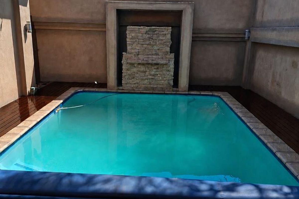 Private courtyard featuring a swimming pool with a stone water feature, surrounded by timber decking and high perimeter walls with electric fencing.