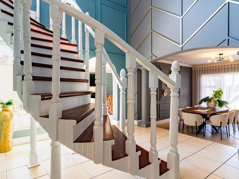 Elegant living area featuring a prominent spiral staircase with wooden treads, decorative wall paneling, and tiled flooring, leading into a formal dining space.