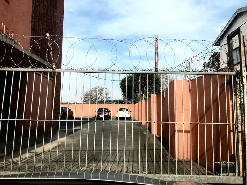 Front entrance view of the townhouse complex featuring a metal security gate, perimeter walling, and razor wire fencing for added security.