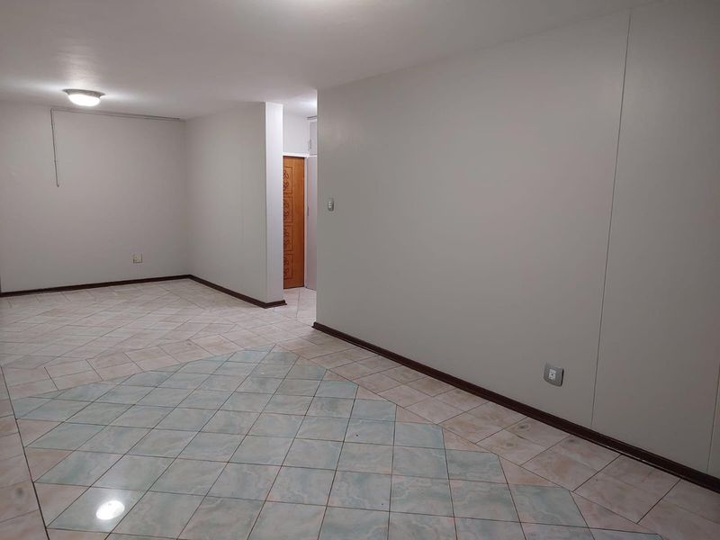 An empty, open-plan living area featuring neutral walls, tiled flooring, and a wooden door leading to an adjacent space.