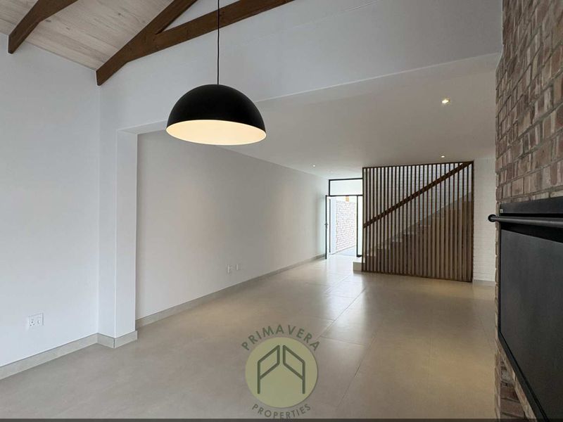 Spacious open-plan living area featuring a vaulted ceiling with exposed timber beams, a brick fireplace, and a modern timber slat staircase screen.