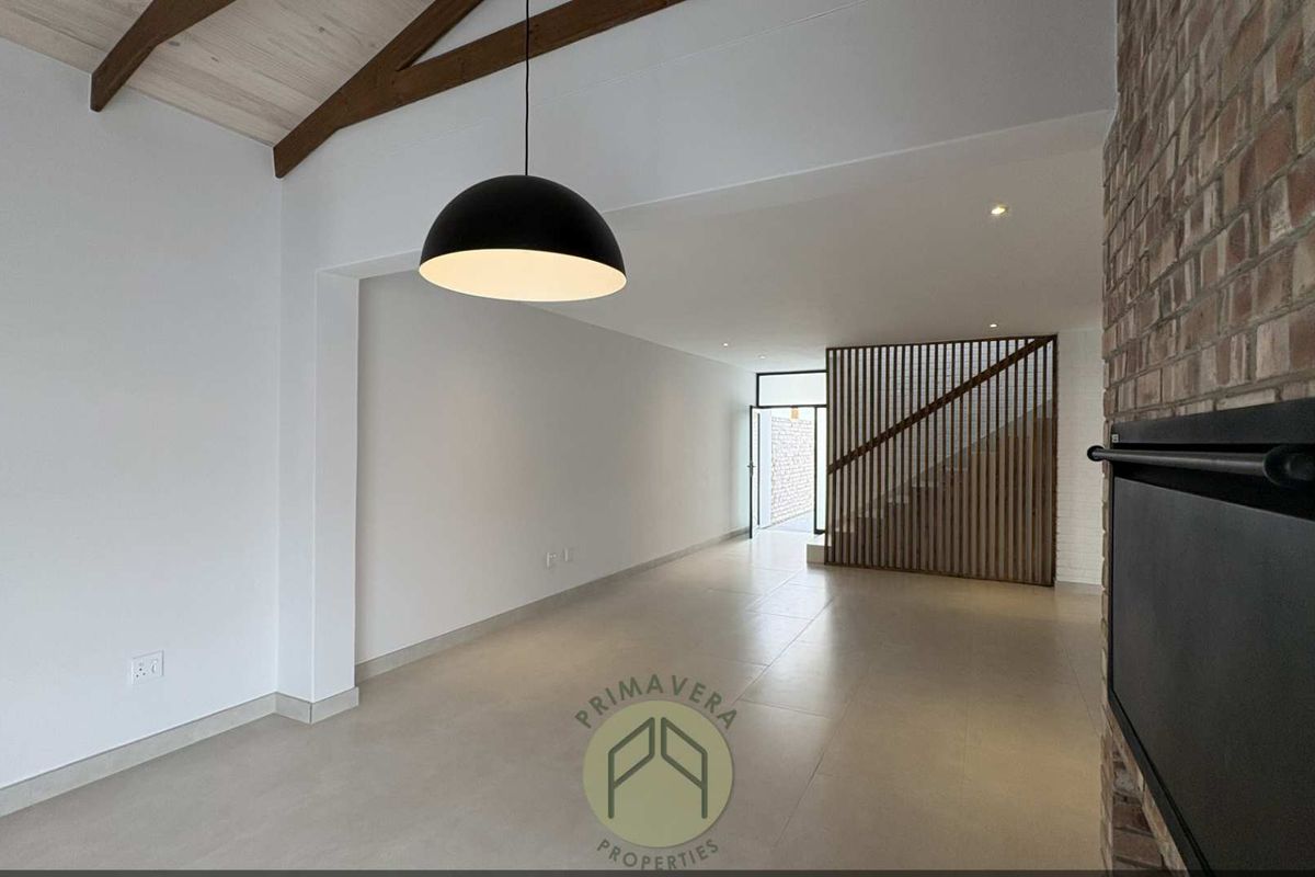 Spacious open-plan living area featuring a vaulted ceiling with exposed timber beams, a brick fireplace, and a modern timber slat staircase screen.