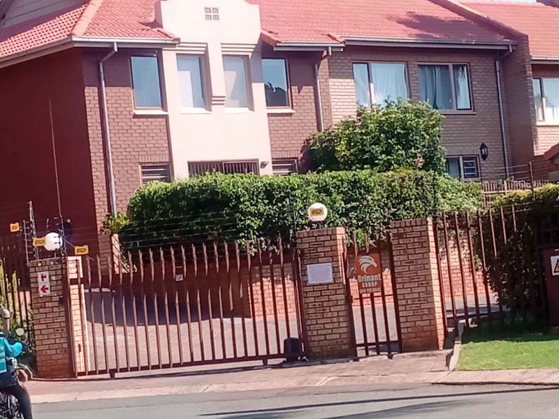Front elevation of a brick townhouse featuring a tiled roof, secure gated entrance, paved driveway, and perimeter electric fencing.