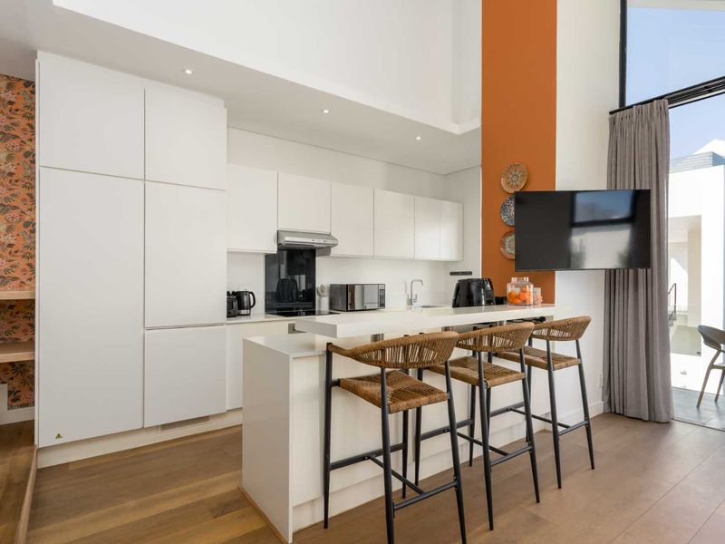 Modern open-plan kitchen featuring sleek white cabinetry, a stone-topped island, and high-quality hardwood flooring, seamlessly connecting to an outdoor balcony area.