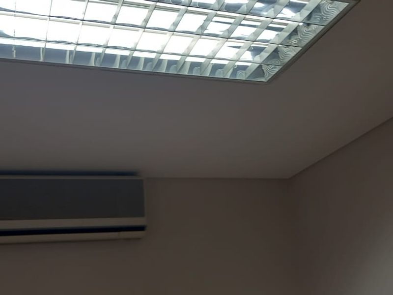 A view of an office ceiling featuring a recessed fluorescent light panel and a wall-mounted air conditioning unit.