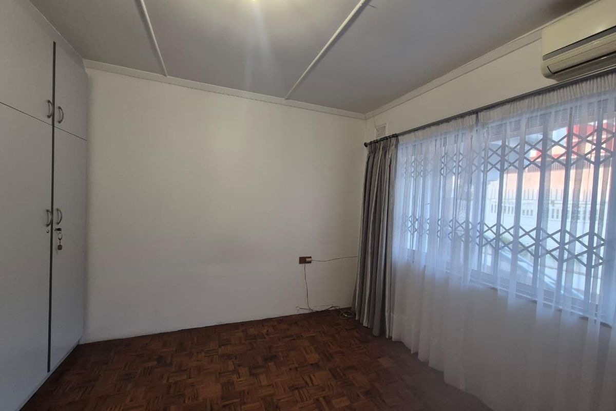 A bright, empty bedroom featuring classic parquet flooring, built-in storage cupboards, and a wall-mounted air conditioning unit.