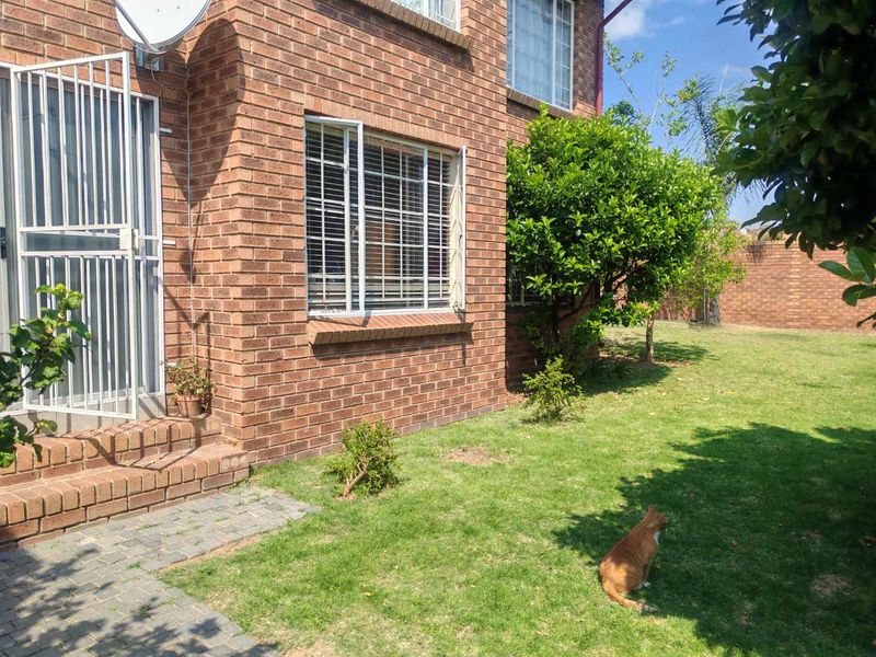 Rear view of the townhouse featuring a face brick facade, security gate, and a private garden area with a paved walkway.