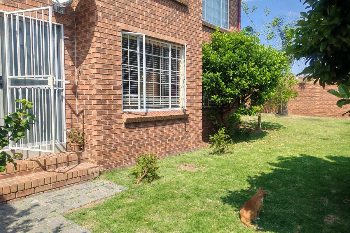 Rear view of the townhouse featuring a face brick facade, security gate, and a private garden area with a paved walkway.