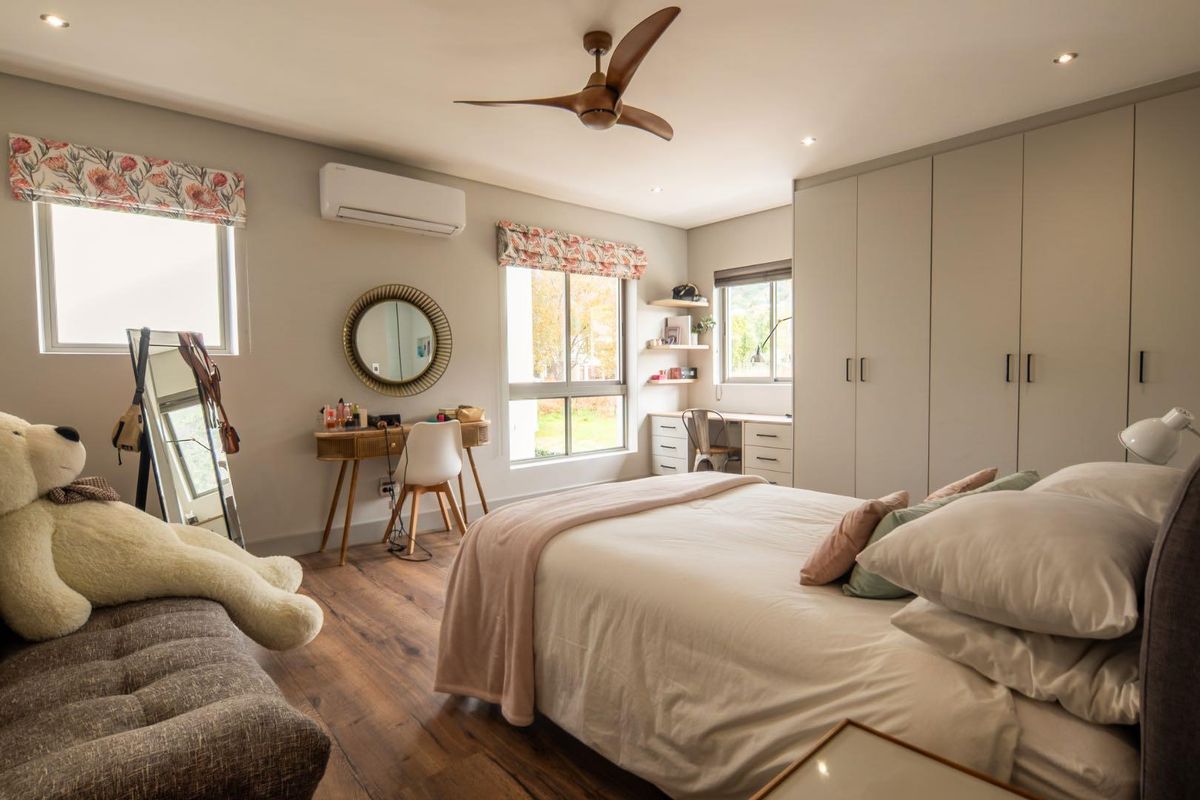 A well-appointed bedroom featuring built-in cupboards, a built-in desk, laminate flooring, a ceiling fan, and a split-system air conditioner.