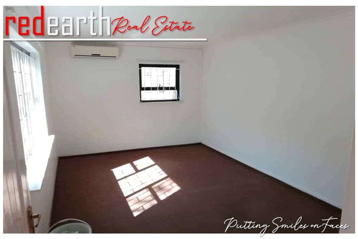 A clean, empty bedroom featuring neutral walls, dark carpeting, and a wall-mounted air conditioning unit.