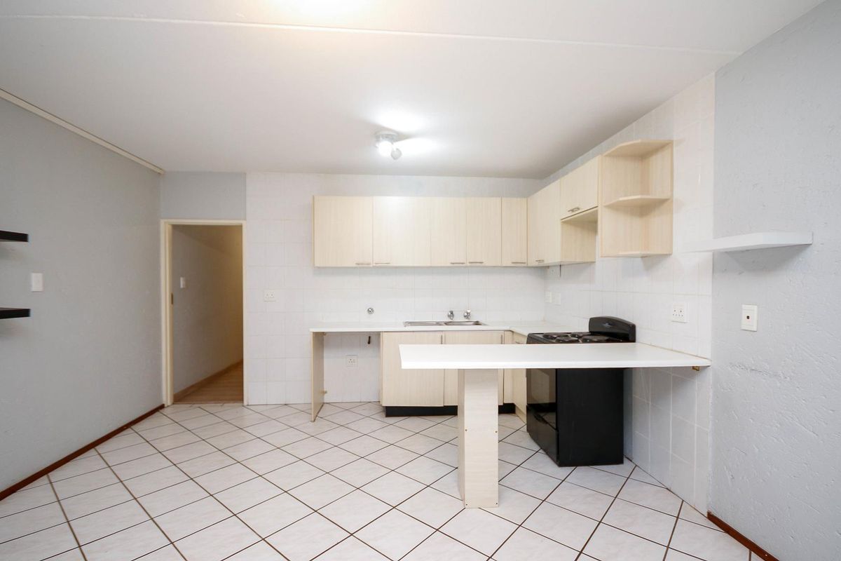 A functional kitchen featuring laminate cabinetry, a tiled splashback, a stainless steel sink, a freestanding stove, and a breakfast bar with tiled flooring.