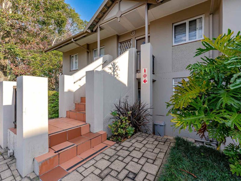 Exterior view of an apartment entrance featuring a paved walkway and a tiled staircase leading to the front door.