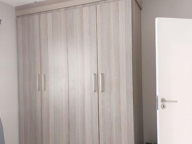 A bedroom featuring a large, modern wood-finish built-in wardrobe with sleek metal handles and a flush-mount ceiling light.