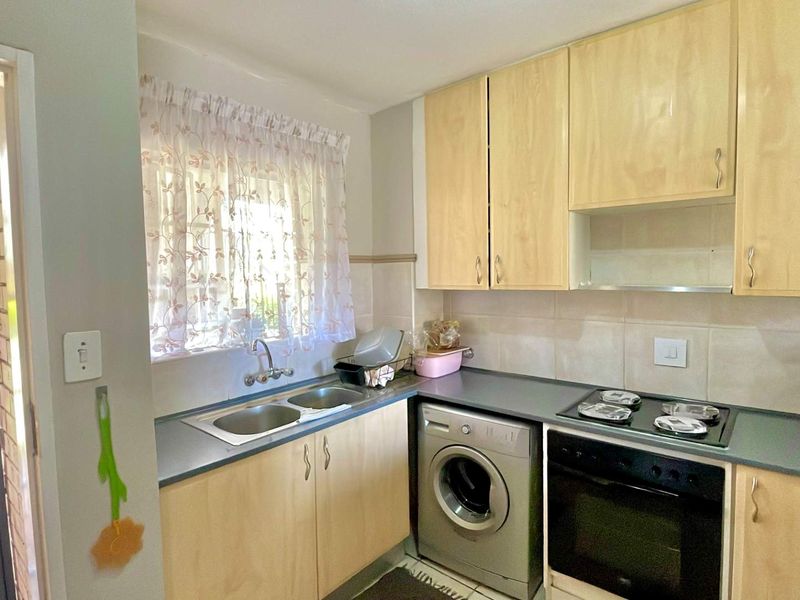 Functional kitchen featuring light wood cabinetry, laminate countertops, built-in oven, electric hob, and a double bowl sink with tiled splashback.