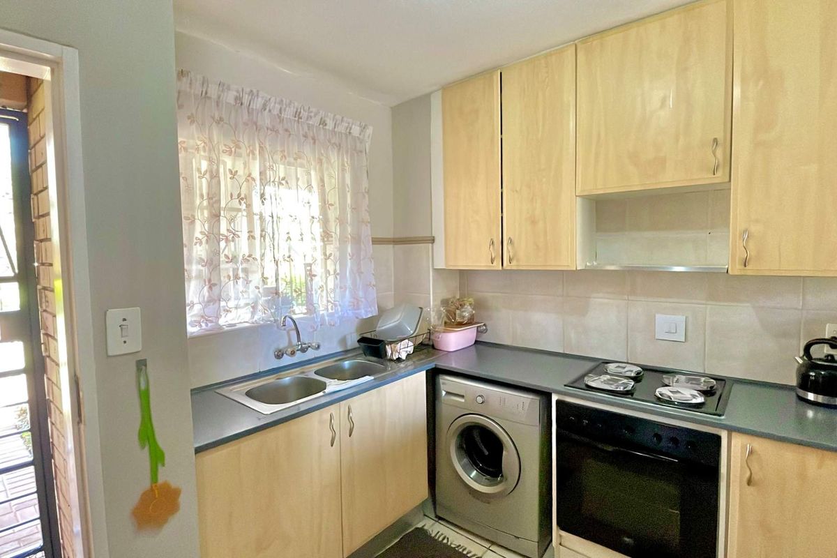 Functional kitchen featuring light wood cabinetry, laminate countertops, built-in oven, electric hob, and a double bowl sink with tiled splashback.