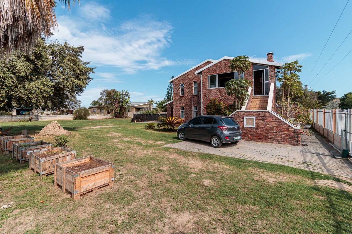 Rear view of a two-story brick house featuring an external staircase, paved driveway, and a spacious garden area.