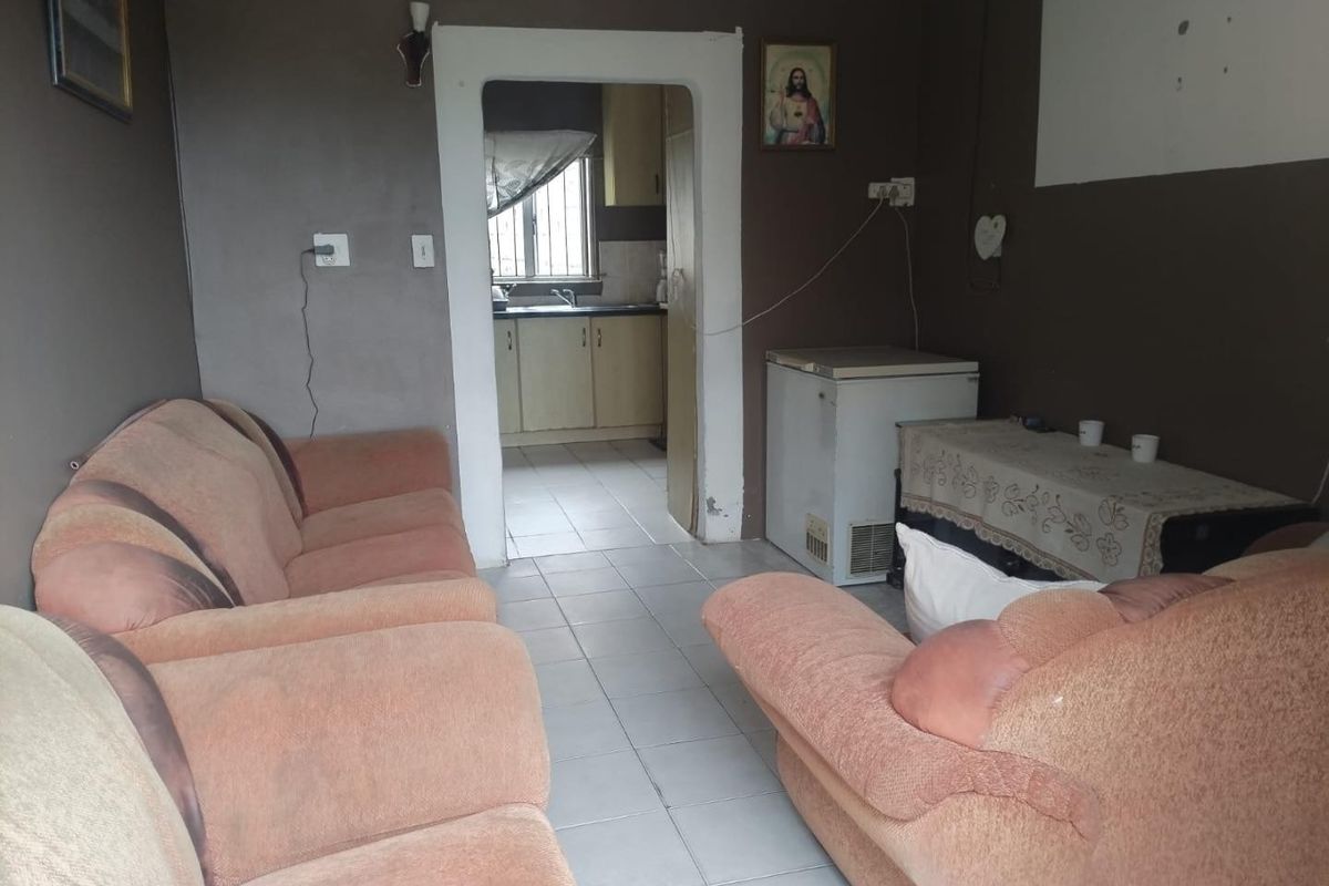 A living room area with tiled flooring and direct access to the kitchen, featuring neutral wall tones and standard electrical fixtures.