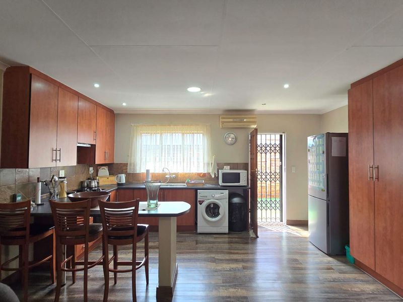 A functional kitchen featuring wood-finish cabinetry, laminate countertops, tiled backsplash, and integrated laundry appliances with direct access to an outdoor area.