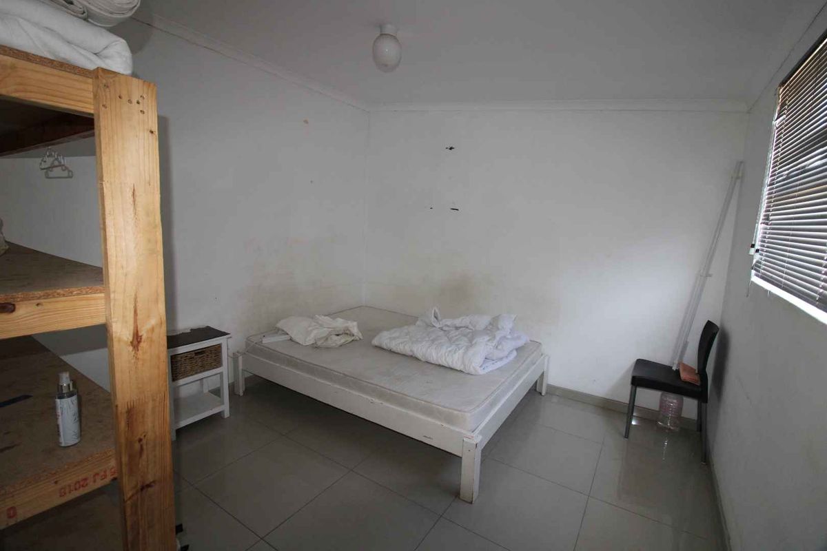 A simple bedroom featuring tiled flooring, a window with fitted blinds, and basic ceiling lighting.