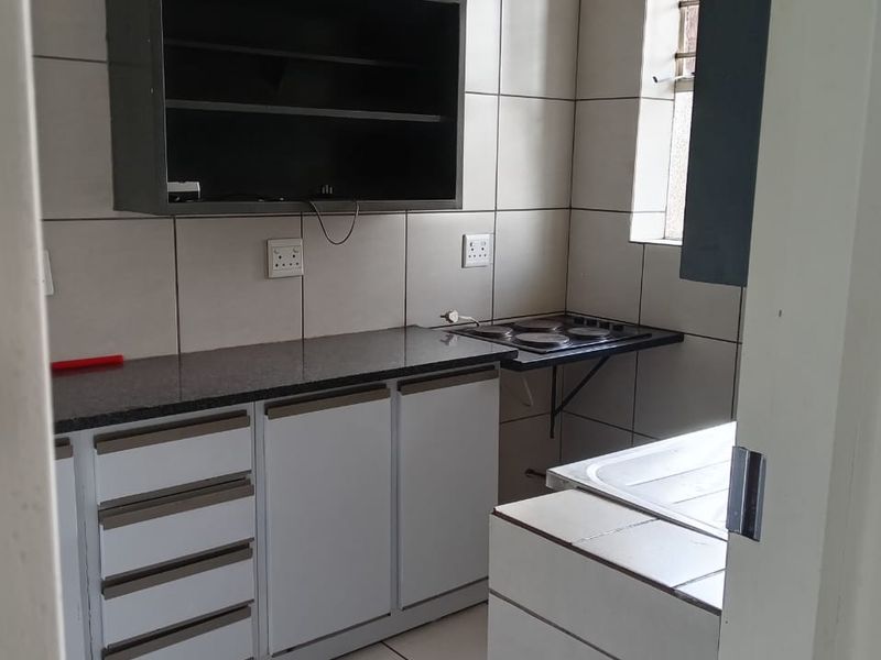 A functional kitchen featuring built-in cabinetry, granite countertops, an electric hob, and tiled finishes throughout.