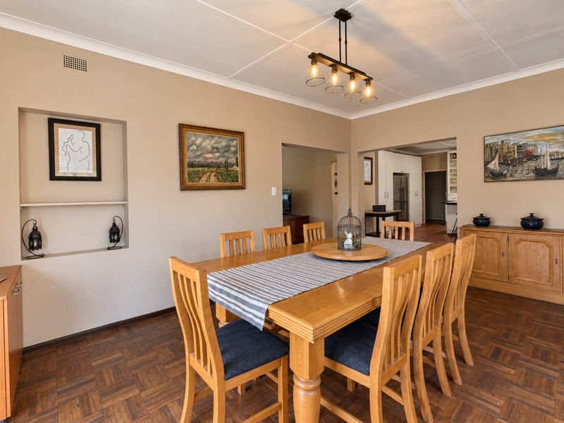 A well-maintained dining room featuring classic parquet flooring, a built-in wall niche, and coved ceilings, with an open-plan flow into the adjacent kitchen area.