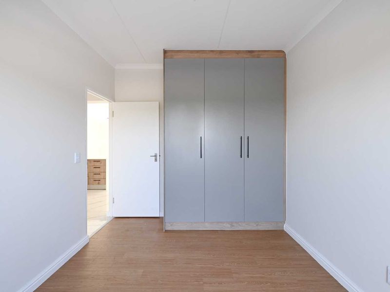 A bright, empty bedroom featuring modern grey built-in cupboards and light wood-look laminate flooring.