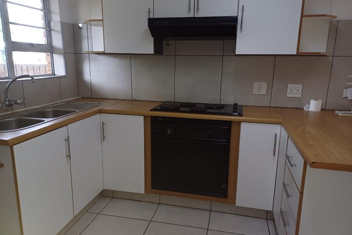 A functional kitchen featuring white cabinetry, laminate countertops, built-in oven and hob, and tiled finishes throughout.