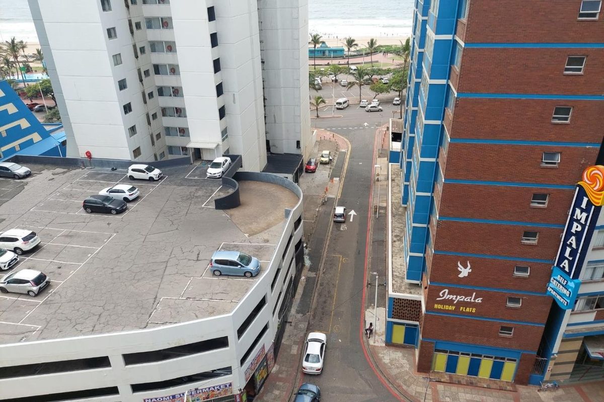 An elevated aerial view showing surrounding apartment buildings, a parking structure, and a street leading toward the beach.