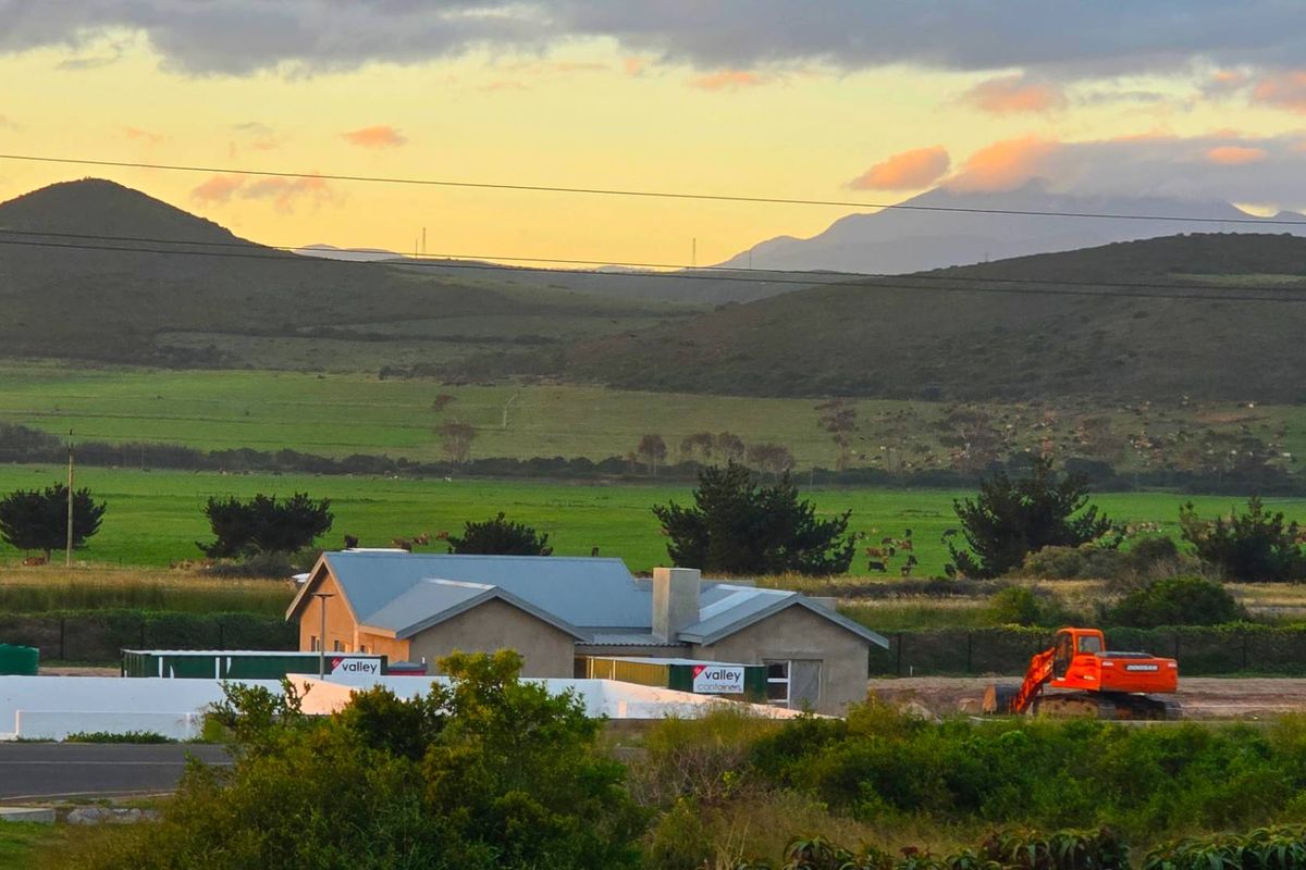 An elevated view of a property under construction, featuring a metal roof and surrounding rural landscape with mountain views.