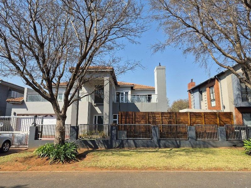 Front elevation of a modern townhouse featuring a tiled roof, chimney, glass balcony railings, and secure metal perimeter fencing with a paved driveway.