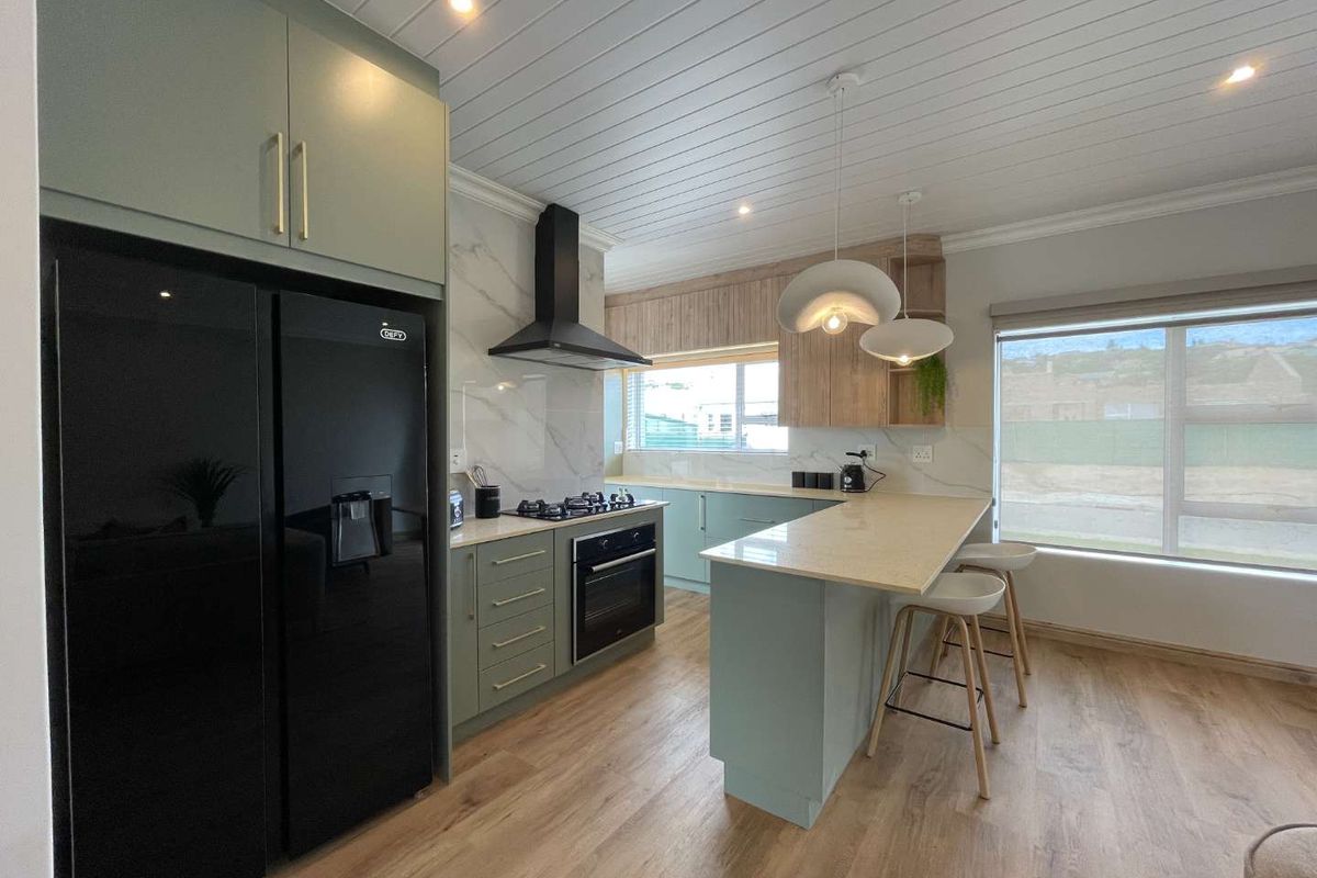 Modern kitchen featuring sage green cabinetry, stone countertops, a breakfast bar, built-in oven, gas hob, and a stylish extractor fan.