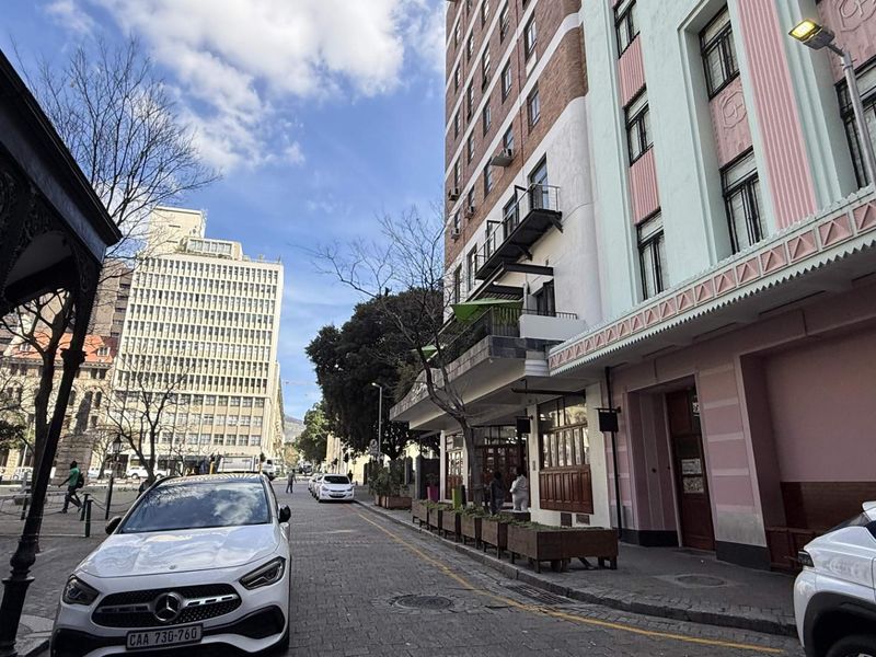 A street-level view of a multi-story urban building with a classic facade, featuring balconies and cobblestone street access.