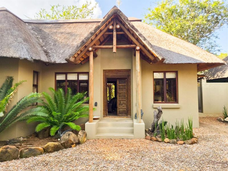 Charming front facade featuring a traditional thatched roof, timber support pillars, and a decorative carved wooden entrance door.