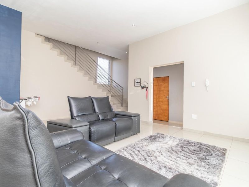 A bright, open-plan living area featuring modern tiled flooring, recessed lighting, and a contemporary staircase with a sleek metal balustrade.