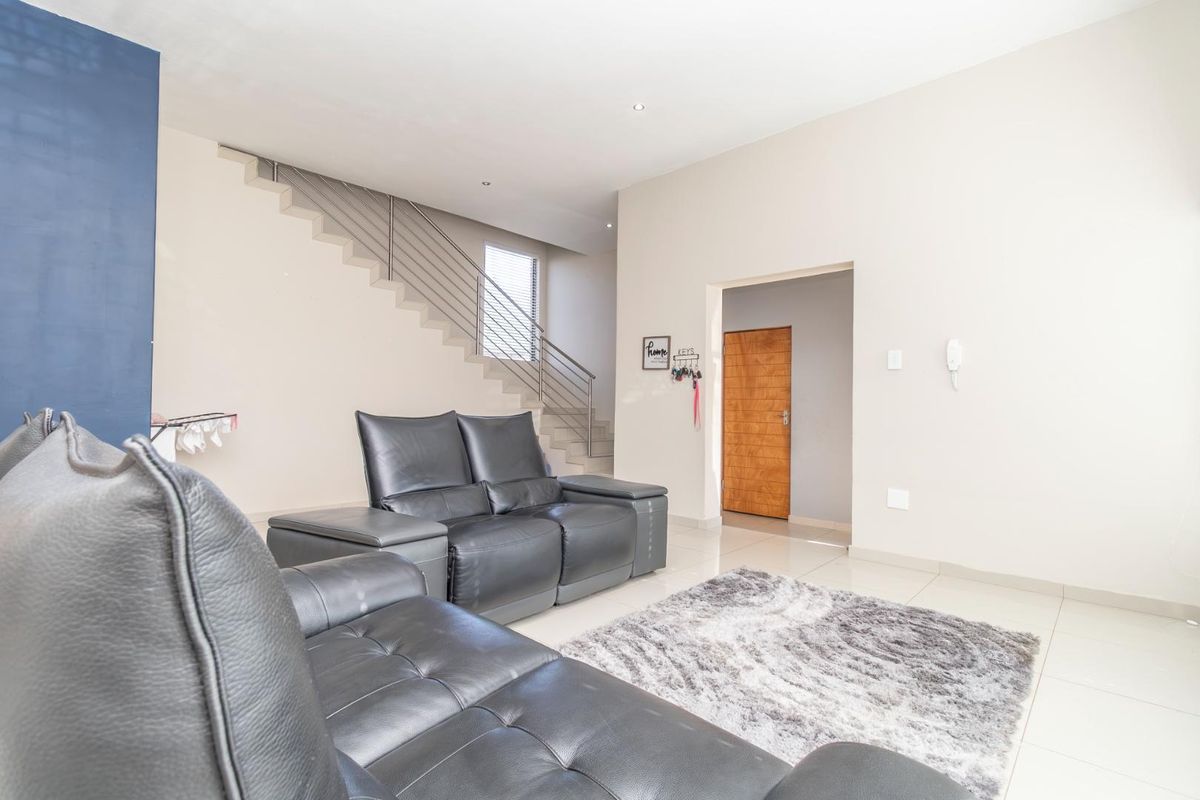 A bright, open-plan living area featuring modern tiled flooring, recessed lighting, and a contemporary staircase with a sleek metal balustrade.