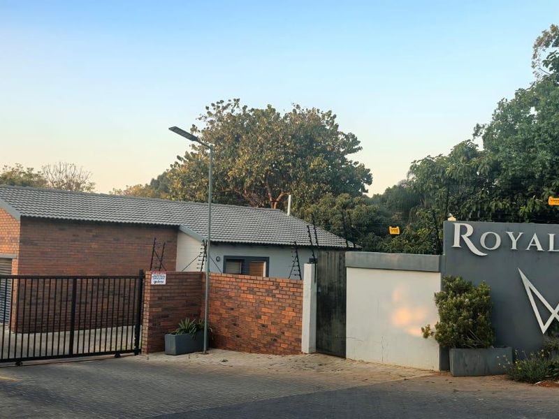 Front entrance view of Royal Ridge complex featuring brick facade buildings, secure gated access, and paved driveway.