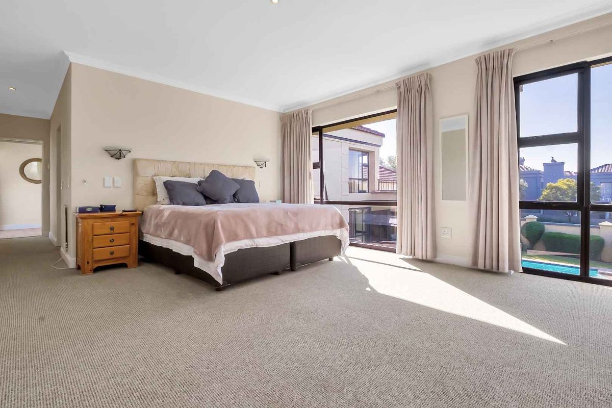 Spacious bedroom featuring large windows with natural light, neutral wall tones, and carpeted flooring, offering a comfortable and bright living space.