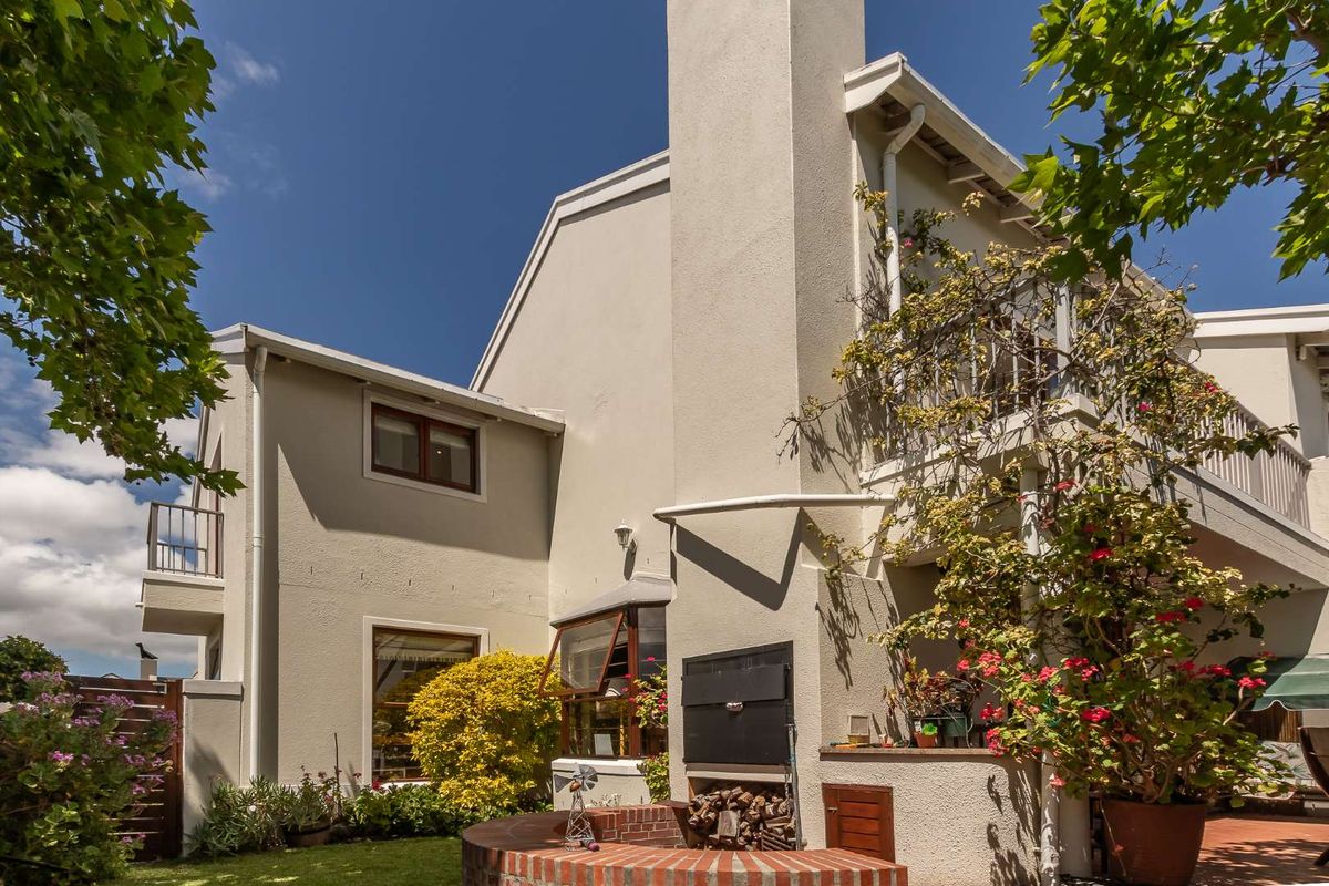 Rear view of the townhouse featuring a built-in braai, chimney stack, and a balcony overlooking the garden area.