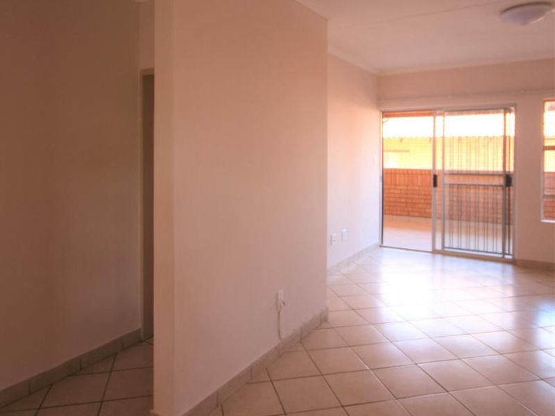 An empty, open-plan living area featuring neutral tiled flooring, coved ceilings, and a sliding glass door providing access to an outdoor balcony.