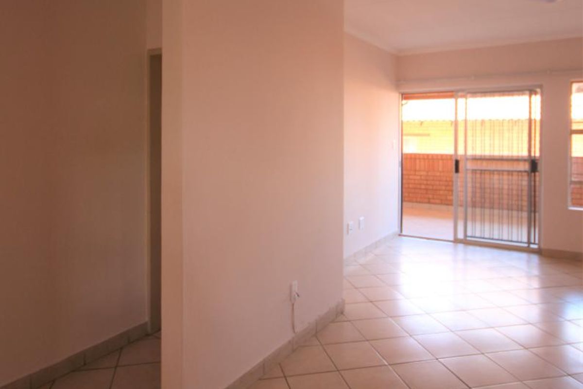 An empty, open-plan living area featuring neutral tiled flooring, coved ceilings, and a sliding glass door providing access to an outdoor balcony.