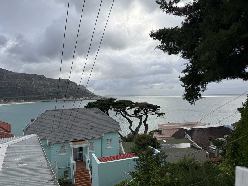Elevated coastal view overlooking the ocean, surrounding residential properties, and distant mountains under a cloudy sky.