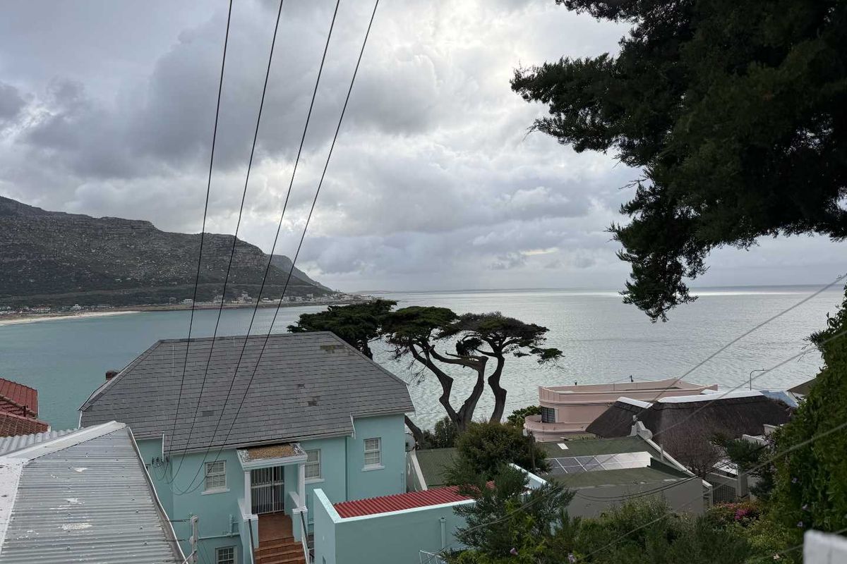 Elevated coastal view overlooking the ocean, surrounding residential properties, and distant mountains under a cloudy sky.