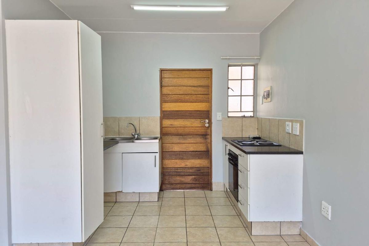 A functional, empty kitchen featuring built-in cabinetry, a stainless steel sink, an integrated oven and hob, and tiled flooring.
