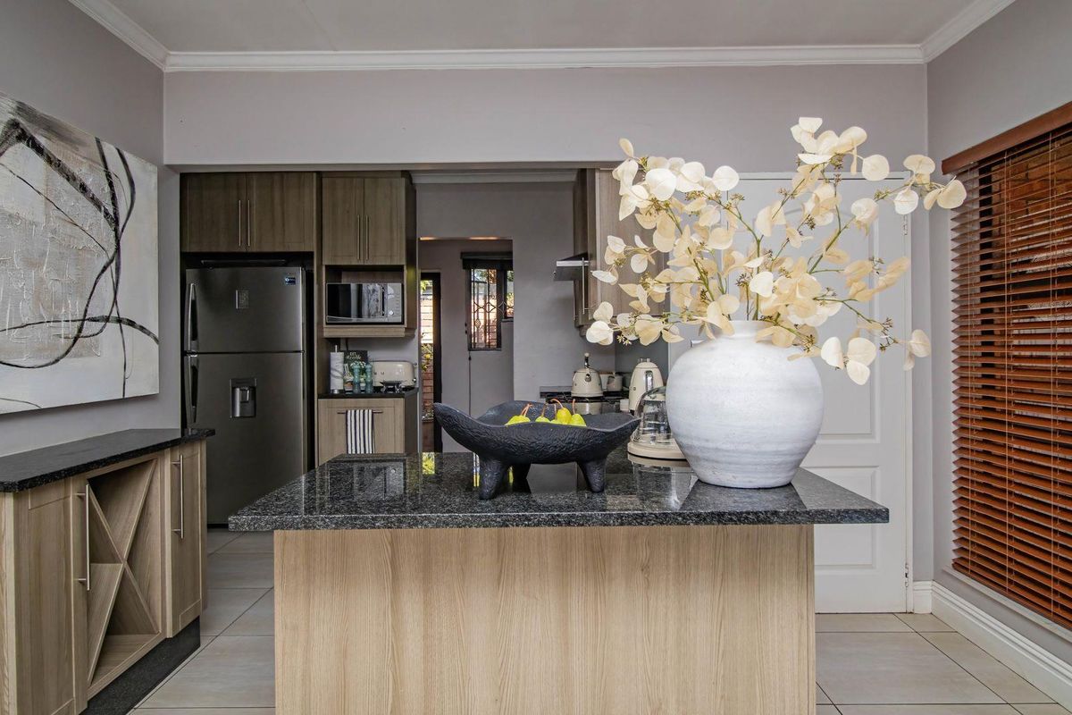 Modern kitchen featuring a central island with granite countertops, light wood-finish cabinetry, and tiled flooring, offering a functional and contemporary cooking space.