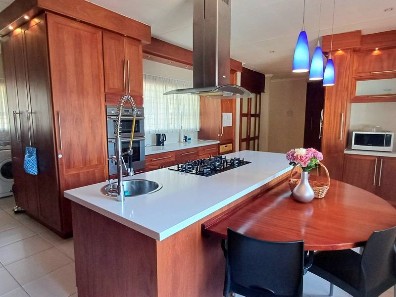 Spacious kitchen featuring extensive wood cabinetry, a large central island with a gas cooktop, integrated appliances, and stone countertops.