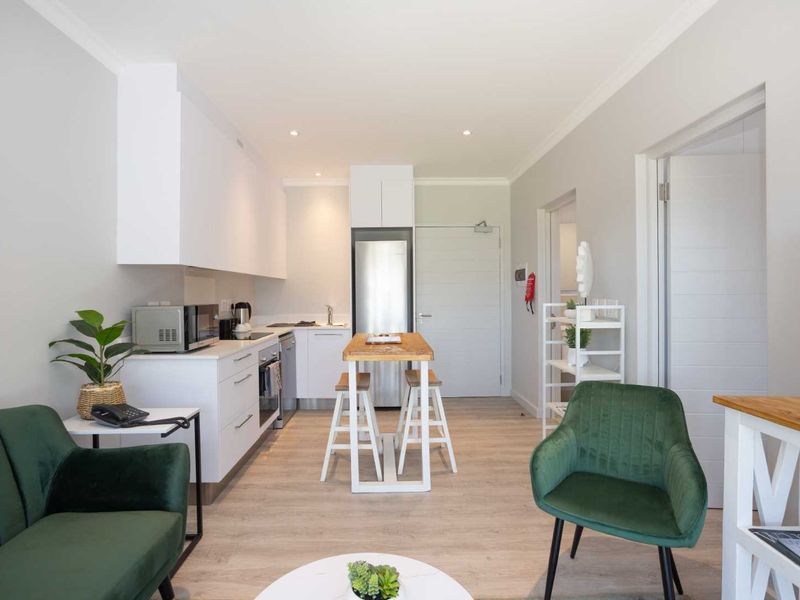 Modern open-plan apartment featuring a compact kitchen with built-in cabinetry, stainless steel appliances, and light wood-look flooring throughout the living area.