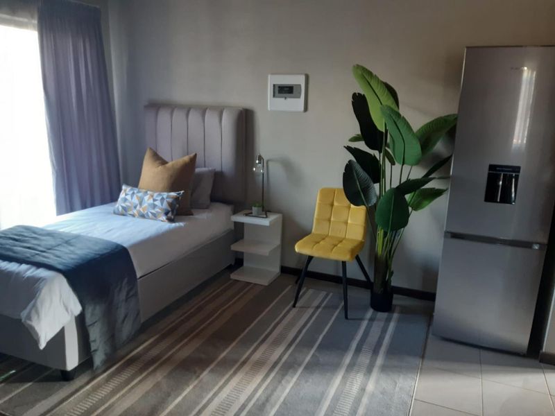 A well-maintained bedroom featuring neutral wall tones, tiled flooring, and large windows with curtain tracks, providing a comfortable and functional living space.